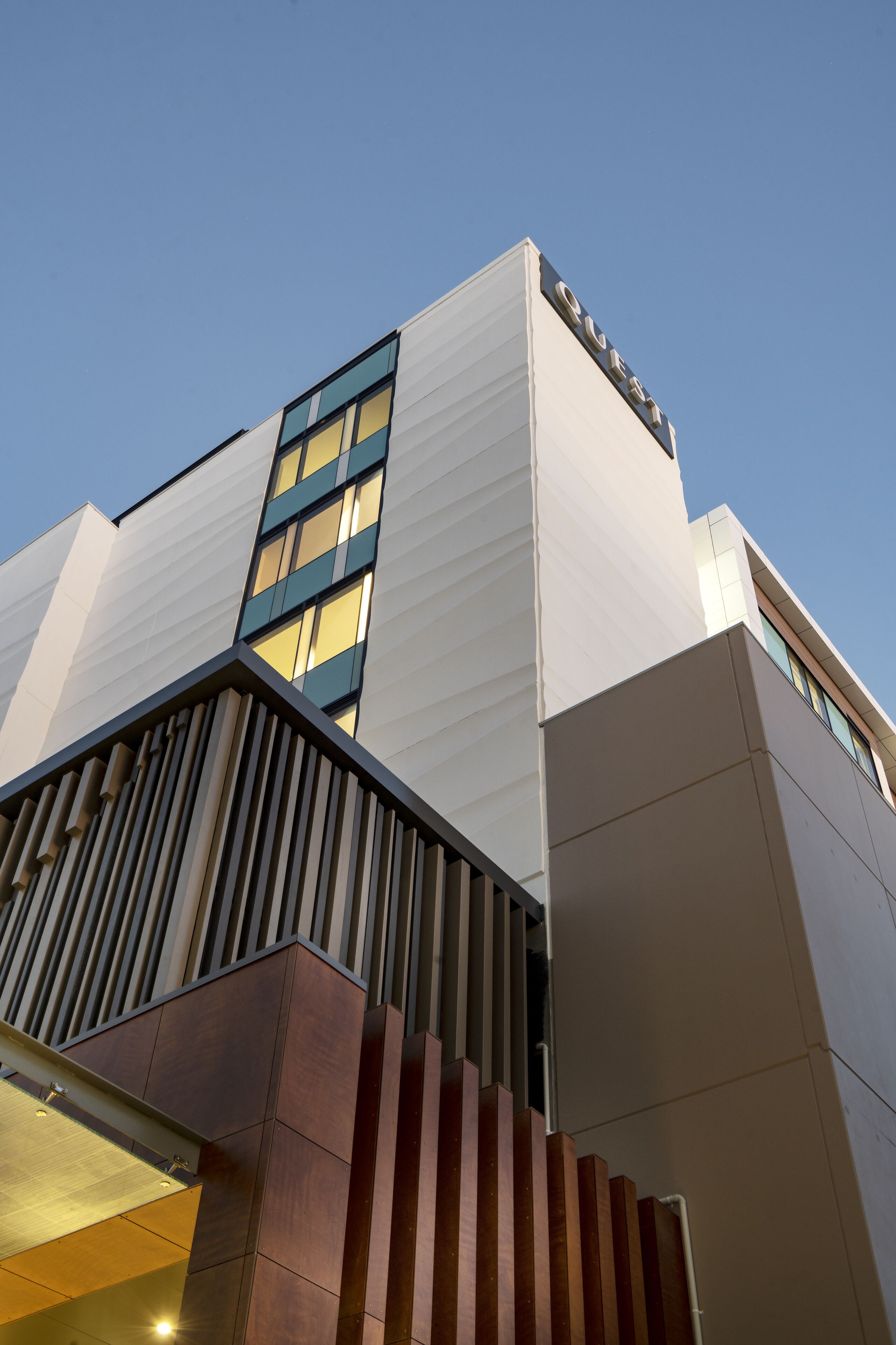 A modern building with a prominent 'QUEEN' sign, a vertical window design, and a structured facade with a mix of materials.