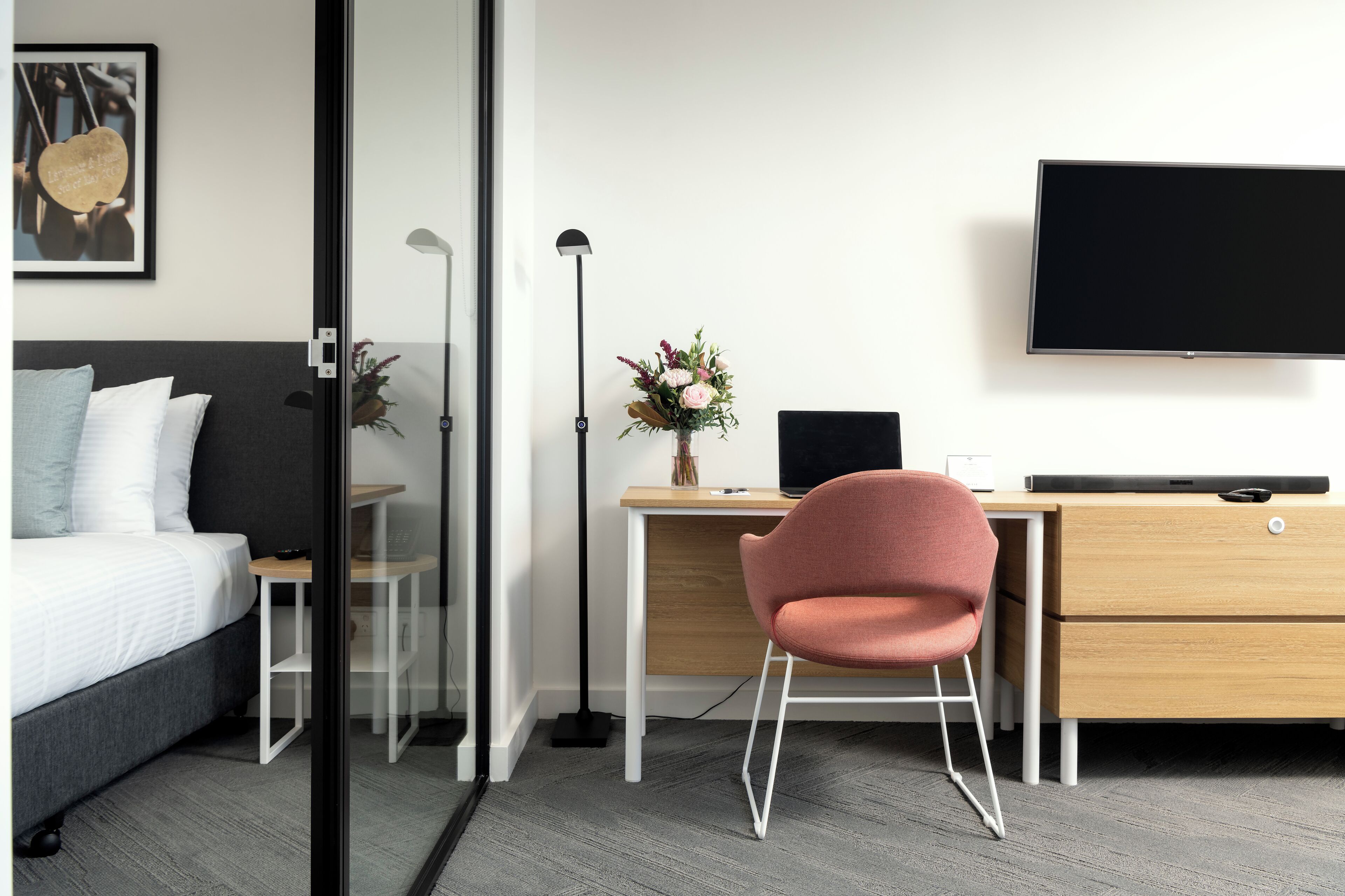Una habitación de hotel moderna con cama, escritorio, silla, televisor y un florero con flores.