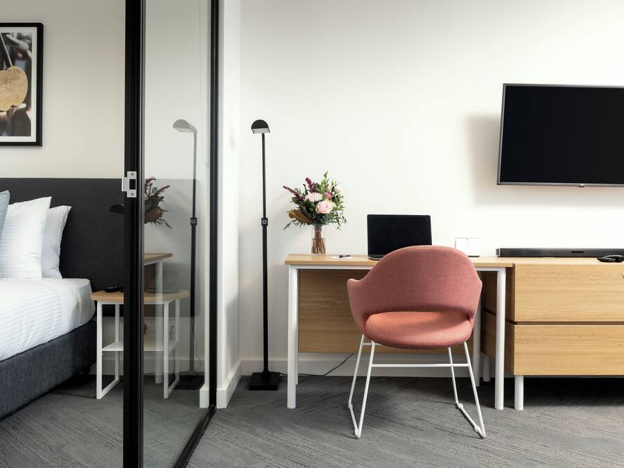 Una habitación de hotel moderna con cama, escritorio, silla, televisor y un florero con flores.
