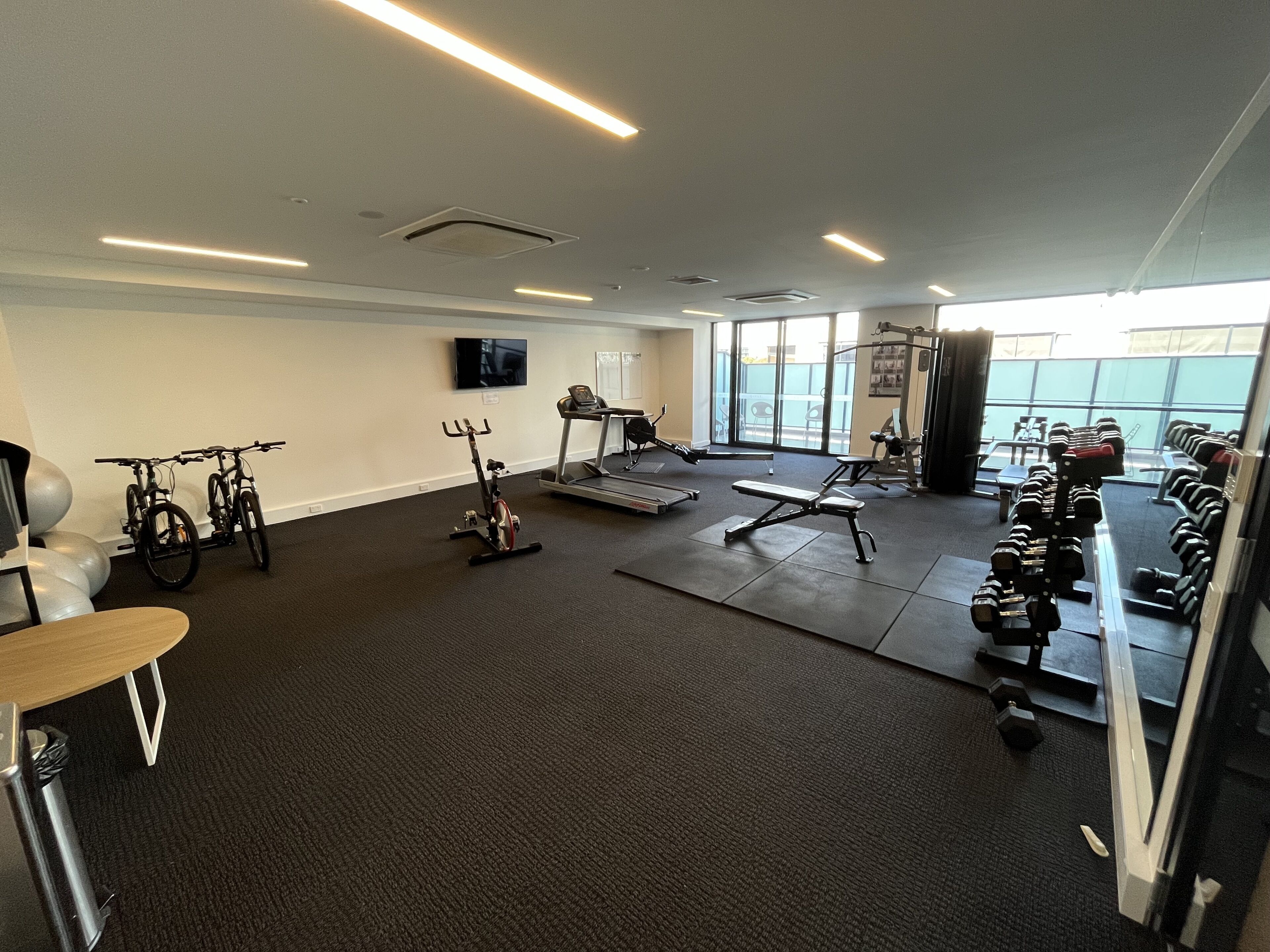 A gym with exercise equipment, a treadmill, and a TV on the wall.