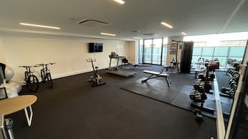 A gym with exercise equipment, a treadmill, and a TV on the wall.