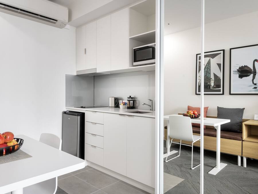 Een moderne keuken met witte kastjes, een magnetron en een spoelbak. Er is een eethoek met een witte tafel en stoelen, en een bank met kussens.