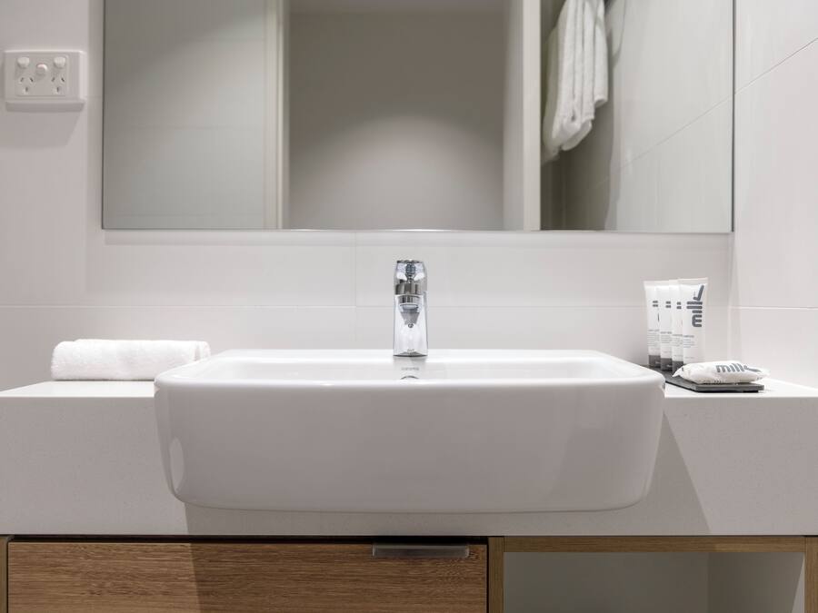 Un baño moderno con un lavamanos blanco, un espejo encima y una toalla al lado.