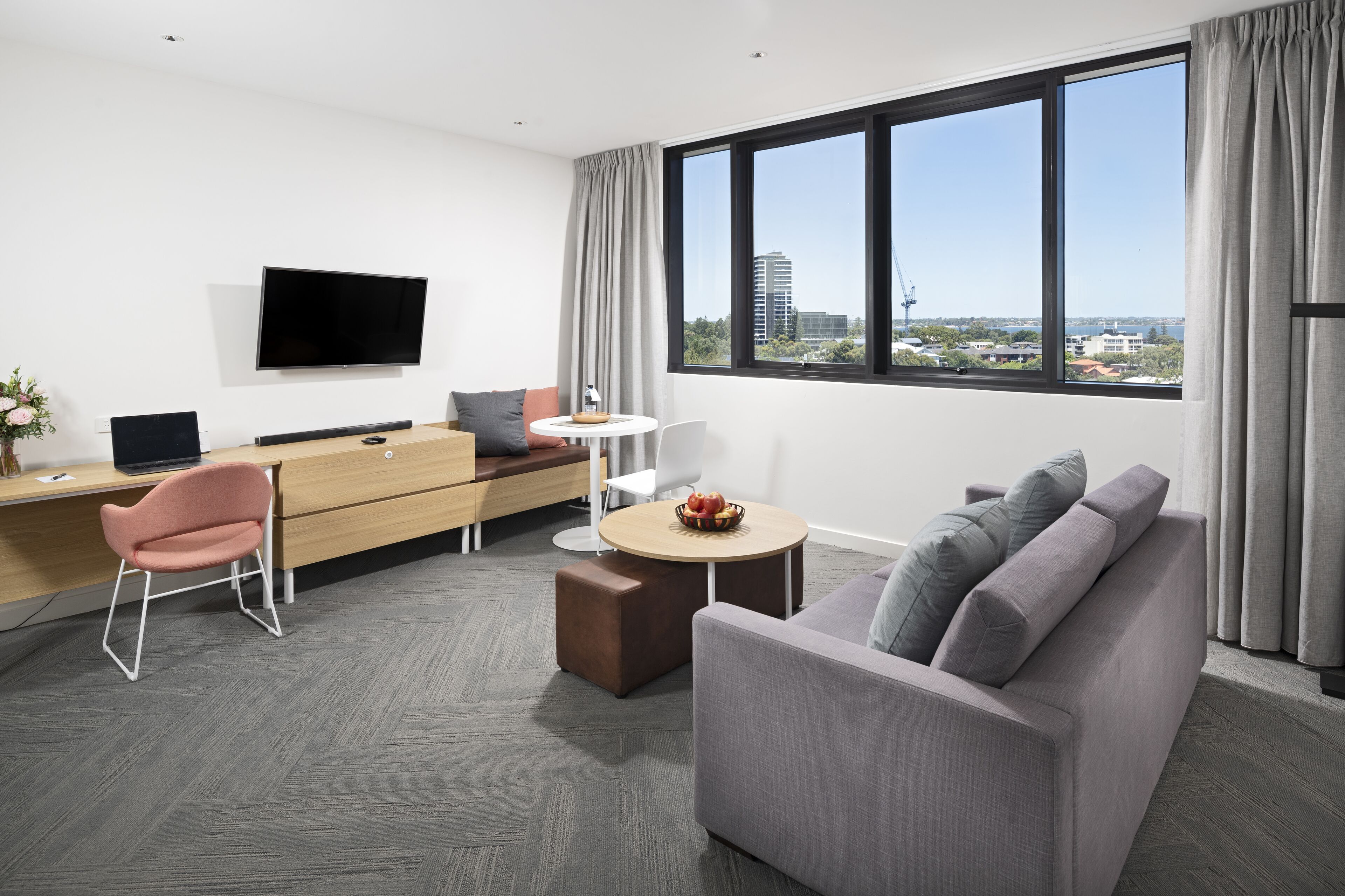 A modern hotel room with a flat-screen TV, a sofa, a desk with a computer, and a dining area.