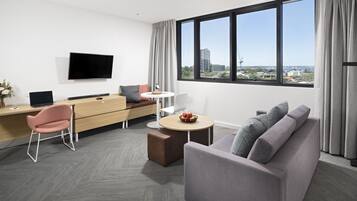 Una habitación de hotel moderna con una televisión de pantalla plana, un sofá, un escritorio con una computadora y una zona de comedor.