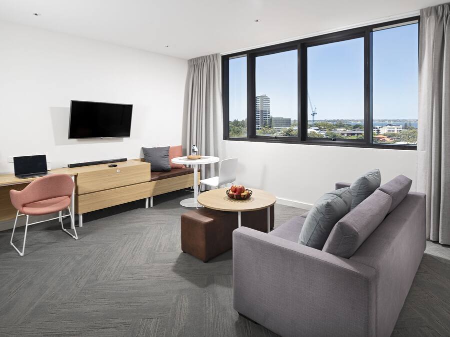Una habitación de hotel moderna con una televisión de pantalla plana, un sofá, un escritorio con una computadora y una zona de comedor.