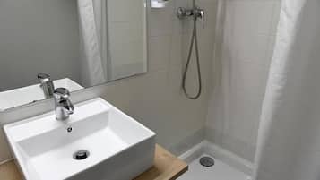 Un baño con lavamanos blanco, un espejo y zona de ducha.
