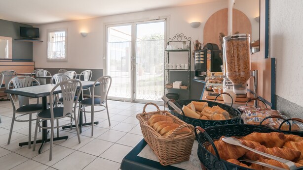 Un espace réservé au petit-déjeuner, avec des tables, des chaises et une variété d’aliments, notamment du pain et des viennoiseries.
