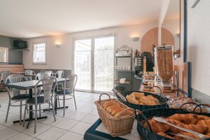 Un espace réservé au petit-déjeuner, avec des tables, des chaises et une variété d’aliments, notamment du pain et des viennoiseries.