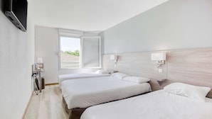 Une chambre d’hôtel avec deux lits, un téléviseur fixé au mur, un bureau avec une lampe et une fenêtre donnant sur l’extérieur.