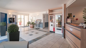 Un hall d’hôtel comprenant un comptoir d’accueil, un distributeur automatique et un escalier menant à d’autres espaces.