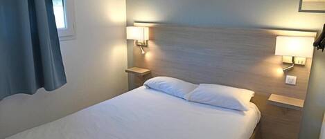 Una cama bien hecha con sábanas blancas en una habitación de hotel. Hay dos lámparas de noche sobre mesitas de madera.