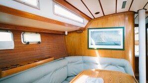 A cabin with a wooden wall, a cushioned bench, a table, and a framed picture of a sailboat. - Sheliak boat and breakfast (Catania)