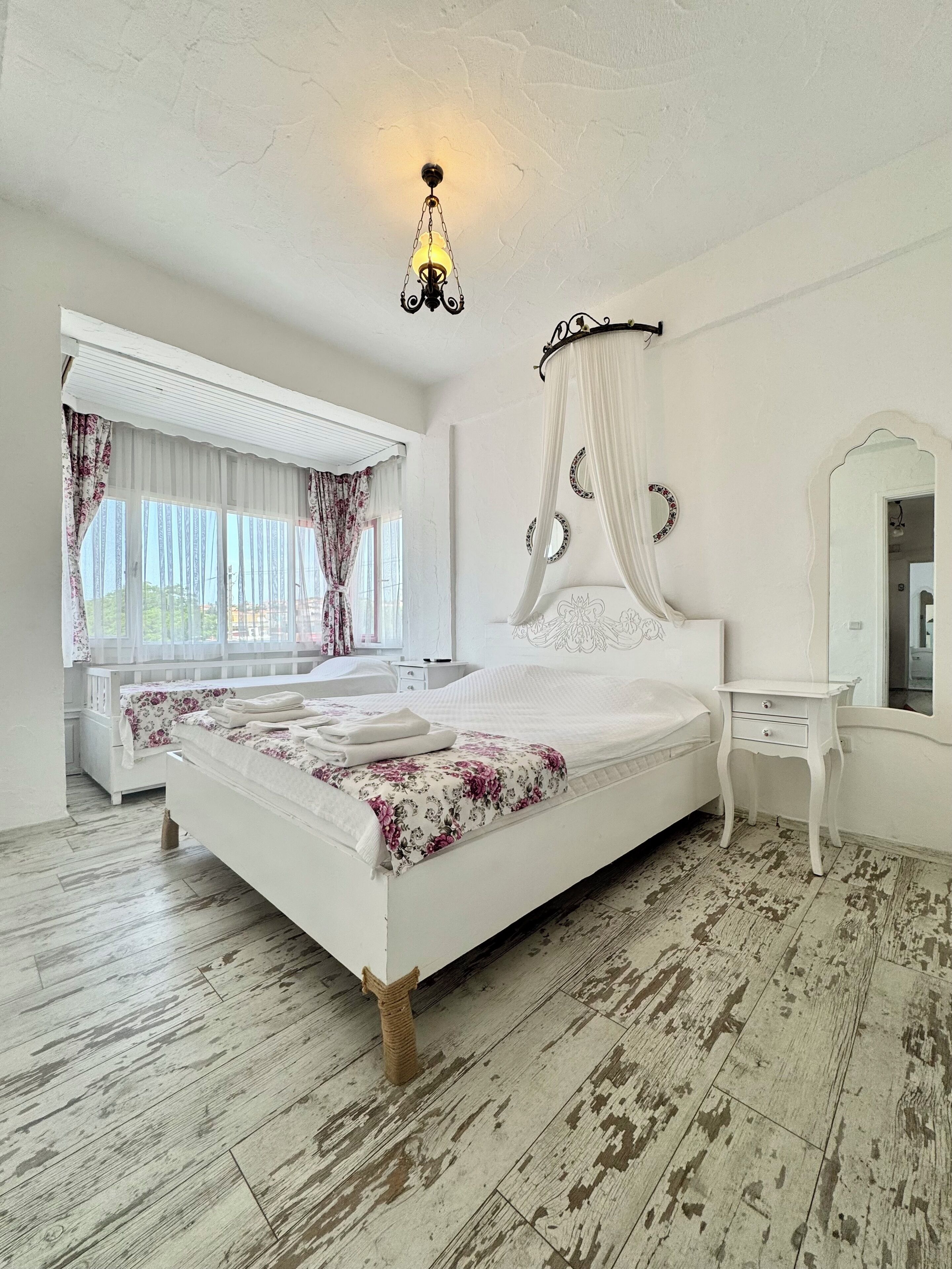 A bedroom with a large bed, a bedside table, a mirror, and a window with curtains.