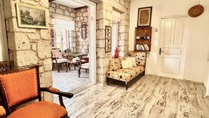 A rustic interior with stone walls, a wooden floor, a sofa, a chair, and a bookshelf. - Aisem By Hire Alacati (Cesme)