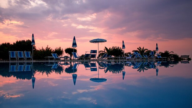 A poolside area with lounge chairs and umbrellas, reflecting in the water. - Agriturismo Ninea (Ricadi)