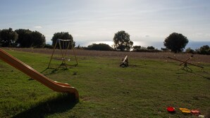 A grassy field with a playground, including a slide and swings, and a view of the sea in the background. - Agriturismo Ninea (Ricadi)