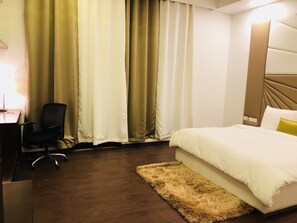 A hotel room with a bed, a desk, a chair, and curtains.