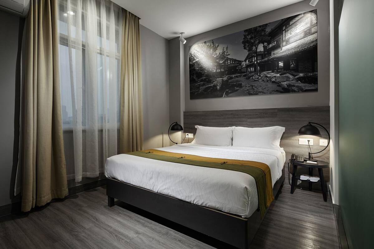Une chambre d’hôtel moderne avec un grand lit, une table de chevet avec une lampe et un tableau accroché au mur.