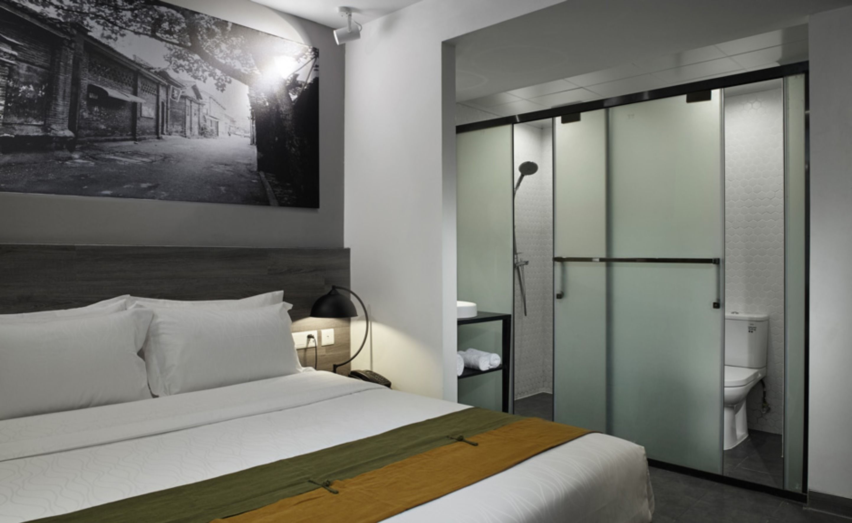 A hotel room with a bed, a nightstand, a lamp, a painting on the wall, and a sliding door leading to a bathroom.