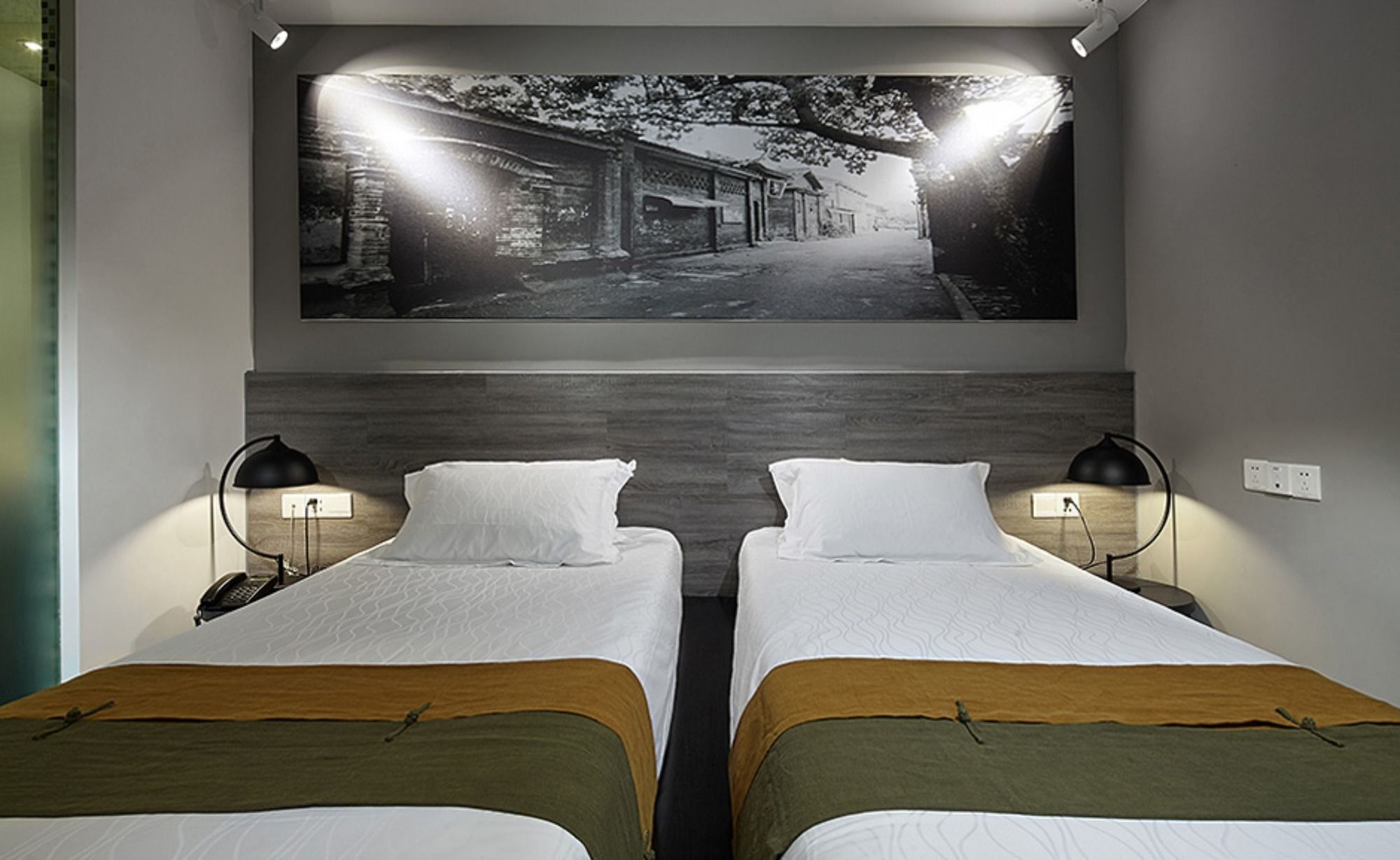 A hotel room with two beds, a large wall-mounted picture, and two bedside lamps.