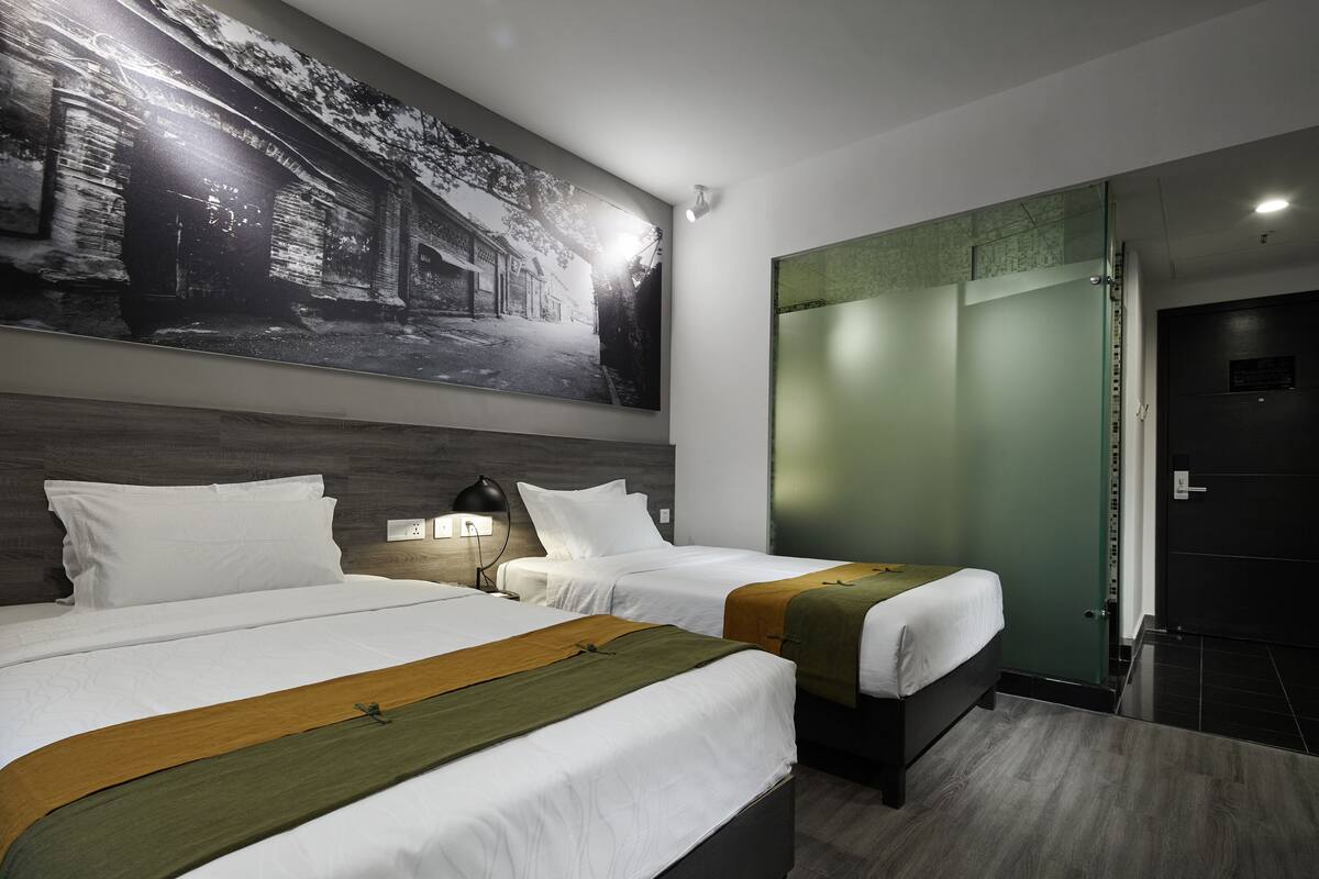 Une chambre d’hôtel avec deux lits, une grande photographie encadrée au mur, une porte verte et une porte noire.