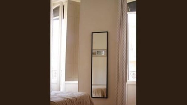 Een slaapkamer met een bed, een grote spiegel en een raam met gordijnen.