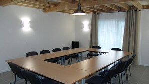 Een vergaderzaal met een lange tafel, zwarte stoelen, een plafondlamp en een raam met gordijnen.