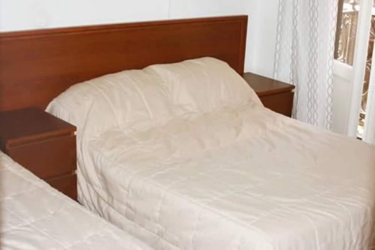 Un lit double avec une tête de lit en bois, une table de chevet et un rideau blanc.