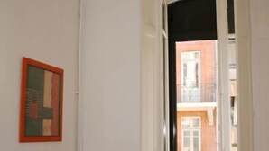 Een interieur gang met een lijstvormig abstract schilderij aan de muur en een uitzicht op een gebouw.