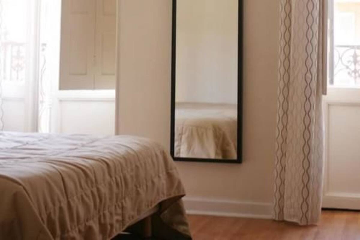 Une chambre à coucher avec un lit, un miroir et une fenêtre avec des rideaux.