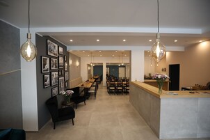 Zona pranzo moderna con un tavolo lungo, sedie e illuminazione a sospensione. Presente una reception con un vaso di fiori.