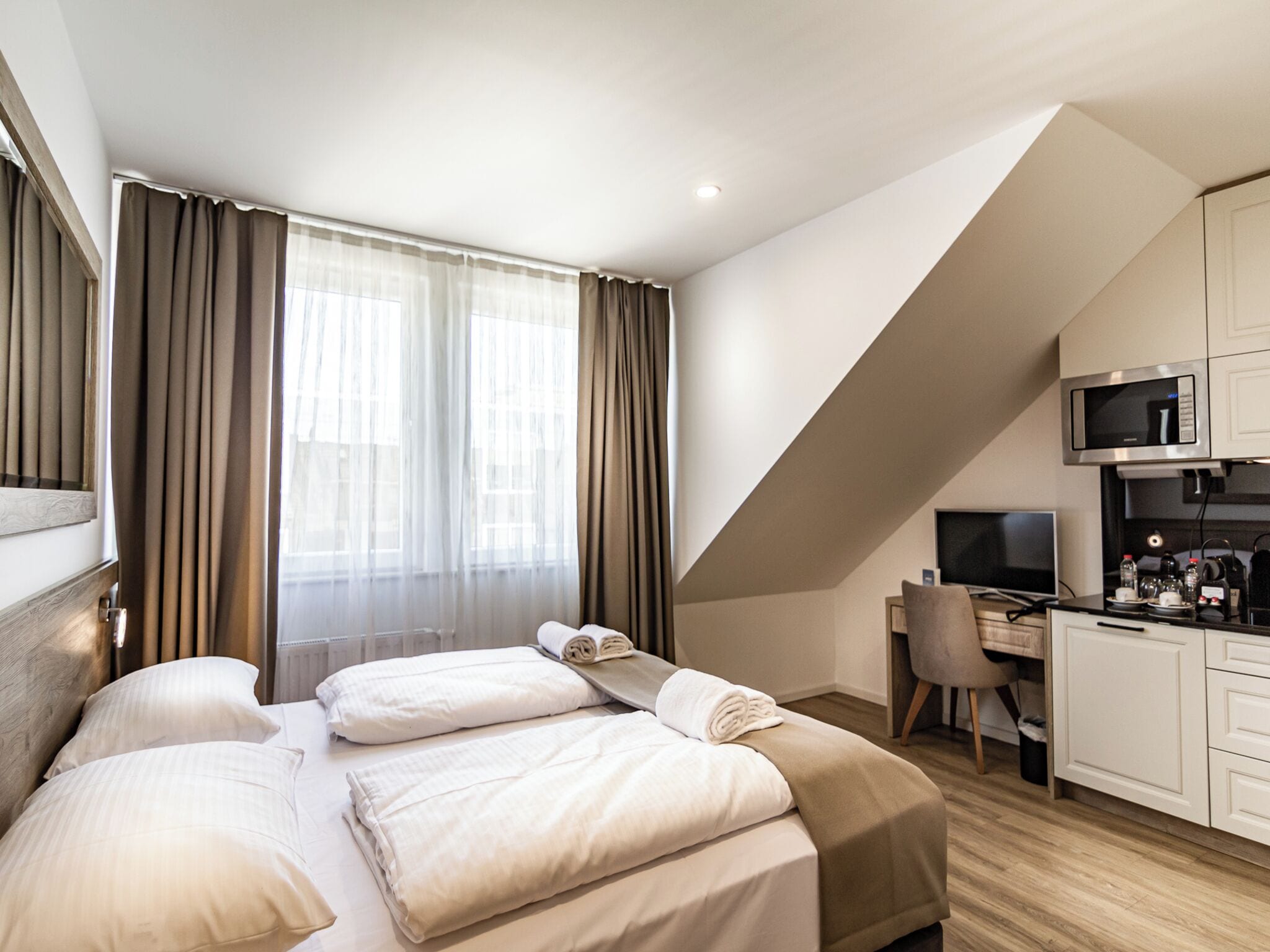 A modern hotel room with a bed, a desk, and a kitchenette.