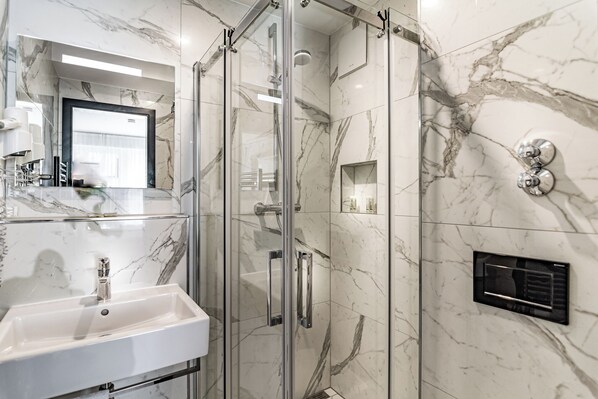A modern bathroom with a glass-enclosed shower, a marble-tiled wall, a white sink, and a built-in heater. - Sleep Inn Düsseldorf (Düsseldorf)