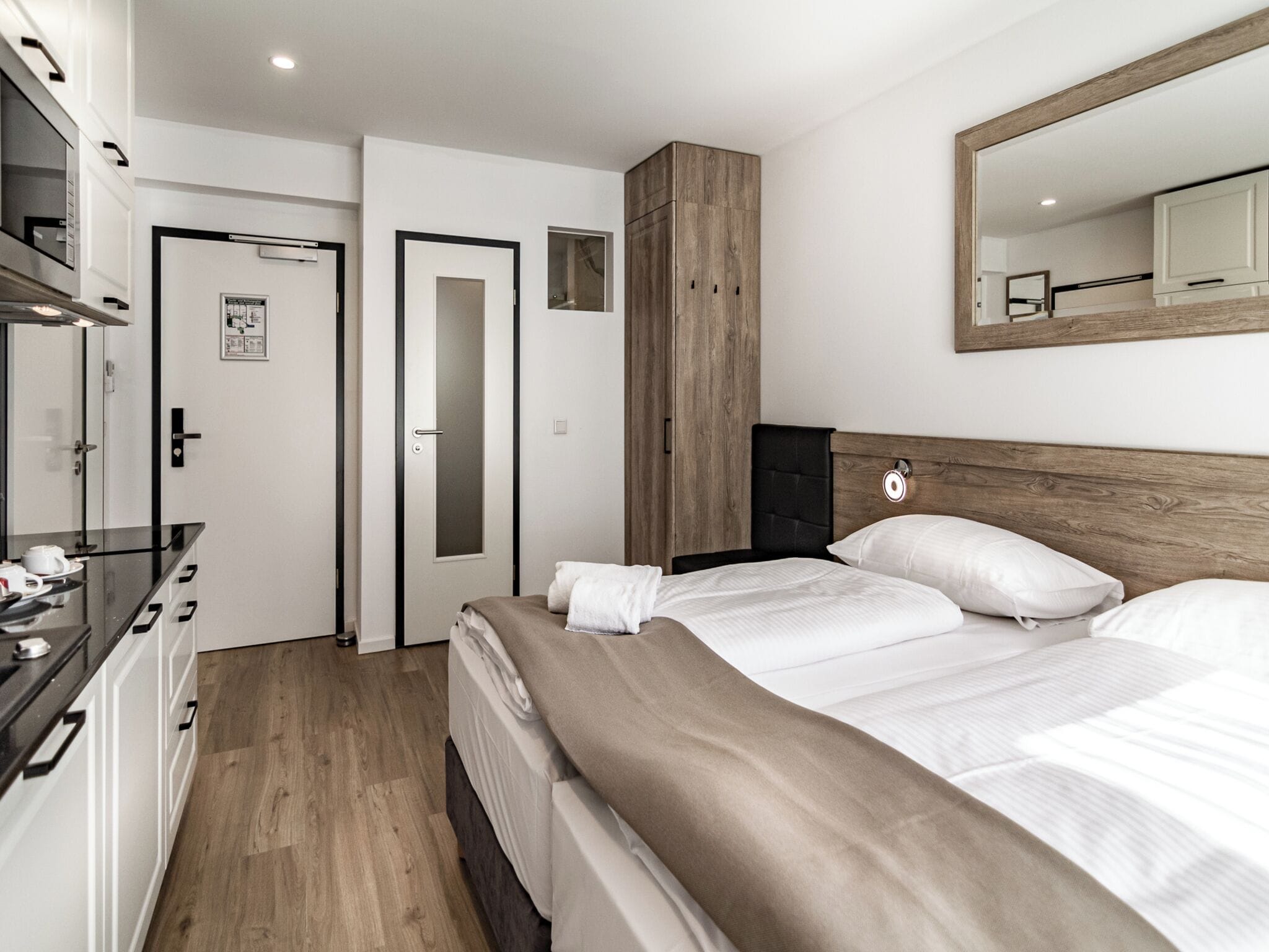 A modern hotel room with a bed, a wardrobe, a mirror, and a small desk with a cup and saucer.