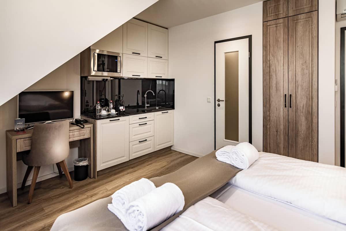 Une chambre d’hôtel compacte comprenant un coin cuisine, un bureau avec une chaise, un lit avec deux oreillers et une armoire.