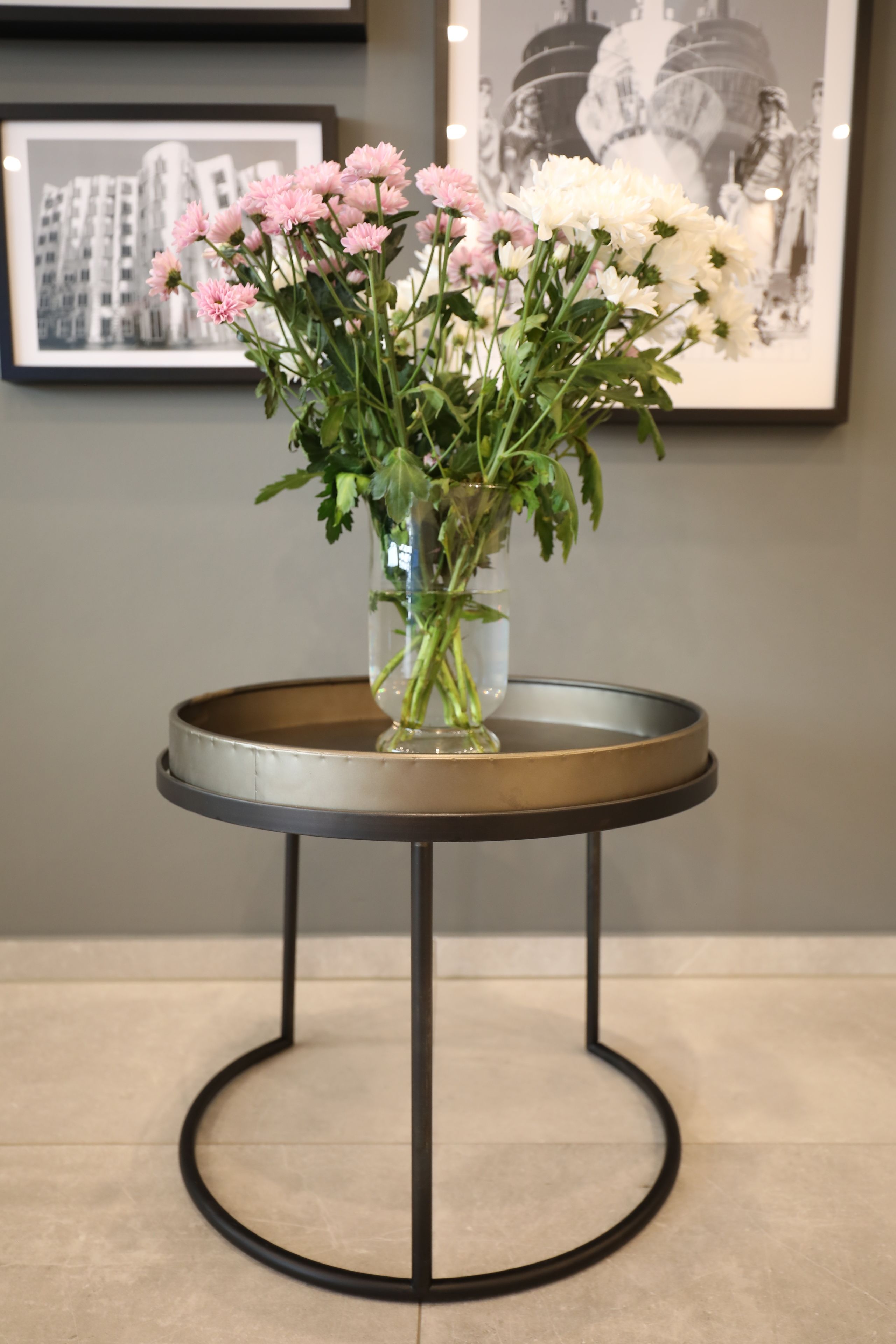 A table with a vase of flowers and a framed picture in the background.