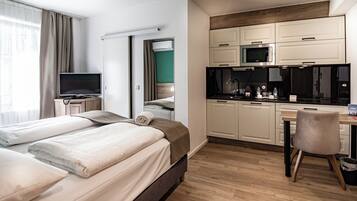 Ein modernes Hotelzimmer mit Bett, Fernseher, Küchenzeile und Schreibtisch.