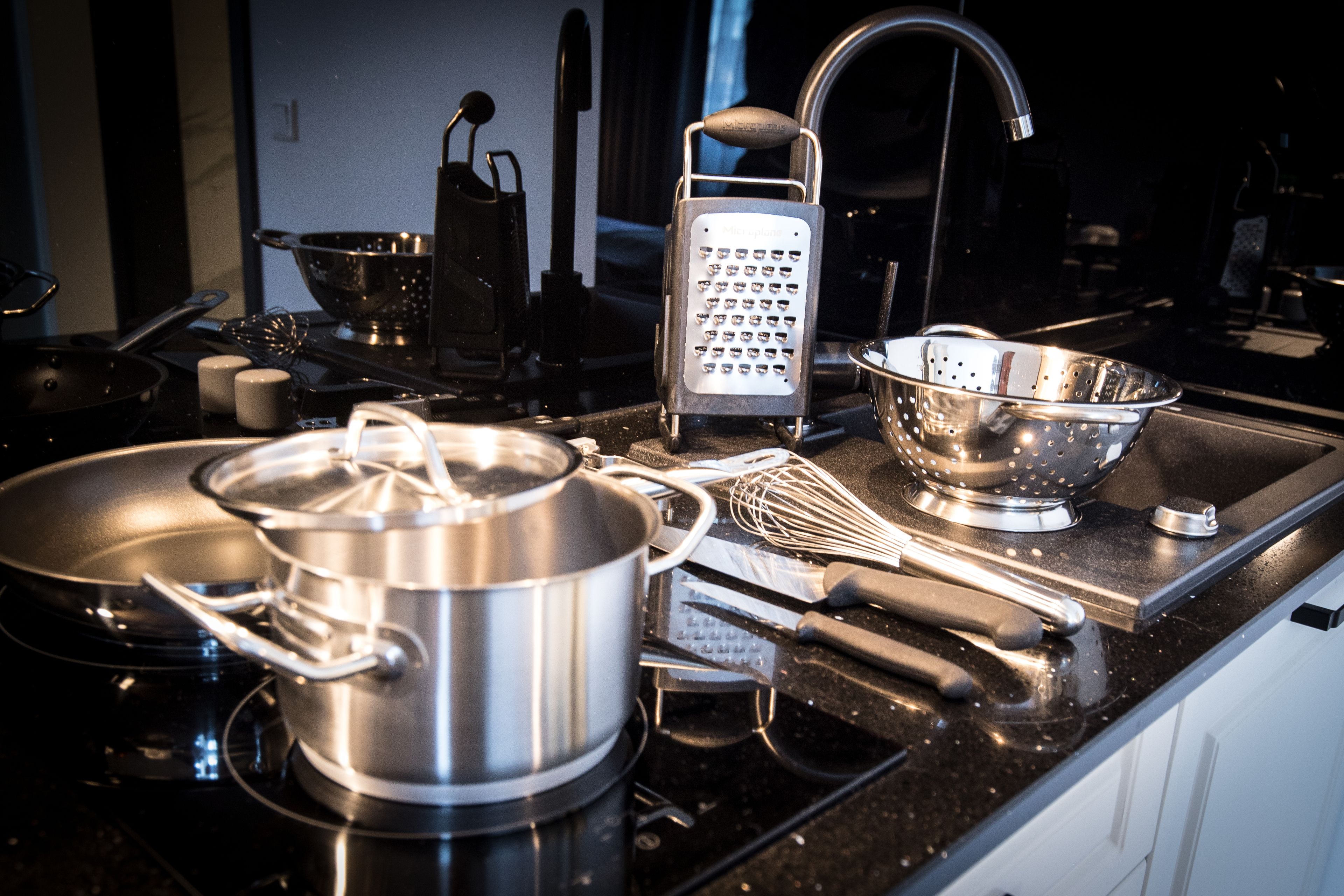 A kitchen with a stove, pots, a grater, a colander, and various utensils.