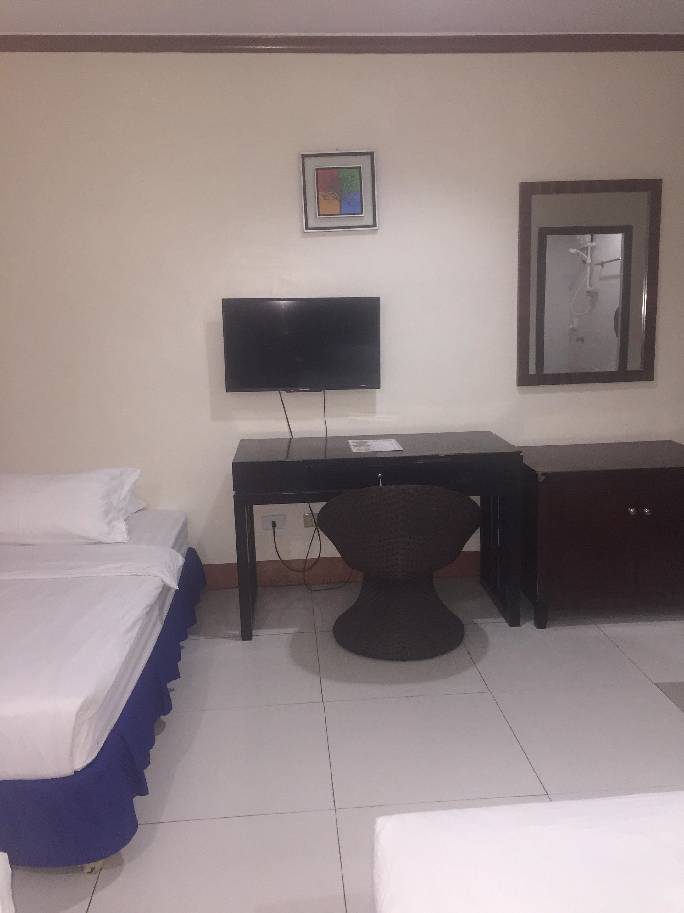 Una habitación de hotel con cama, escritorio, silla, televisor y espejo.