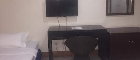 Ein Hotelzimmer mit einem Bett, einem Schreibtisch, einem Sessel, einem Fernseher und einem Spiegel.