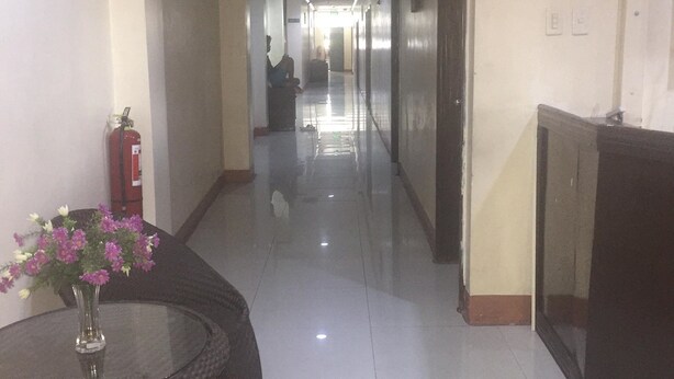 A hotel corridor with a fire extinguisher, a glass table with a vase of flowers, and a door with a red sign.