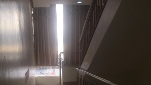 A corridor with a shiny tiled floor, a staircase with wooden railings, and a window with curtains allowing natural light.