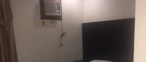 A hotel room with a bed, a nightstand, a wall-mounted air conditioner, and a curtain.