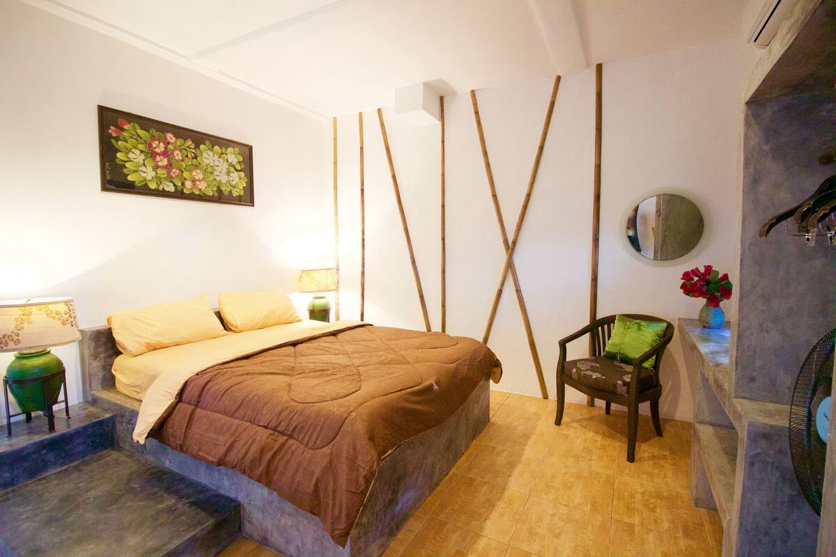 A bedroom with a bed, a chair, a lamp, and a wall-mounted mirror.