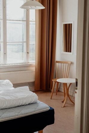 Et hotelværelse med seng, stol, bord og et vindue med gardiner.
