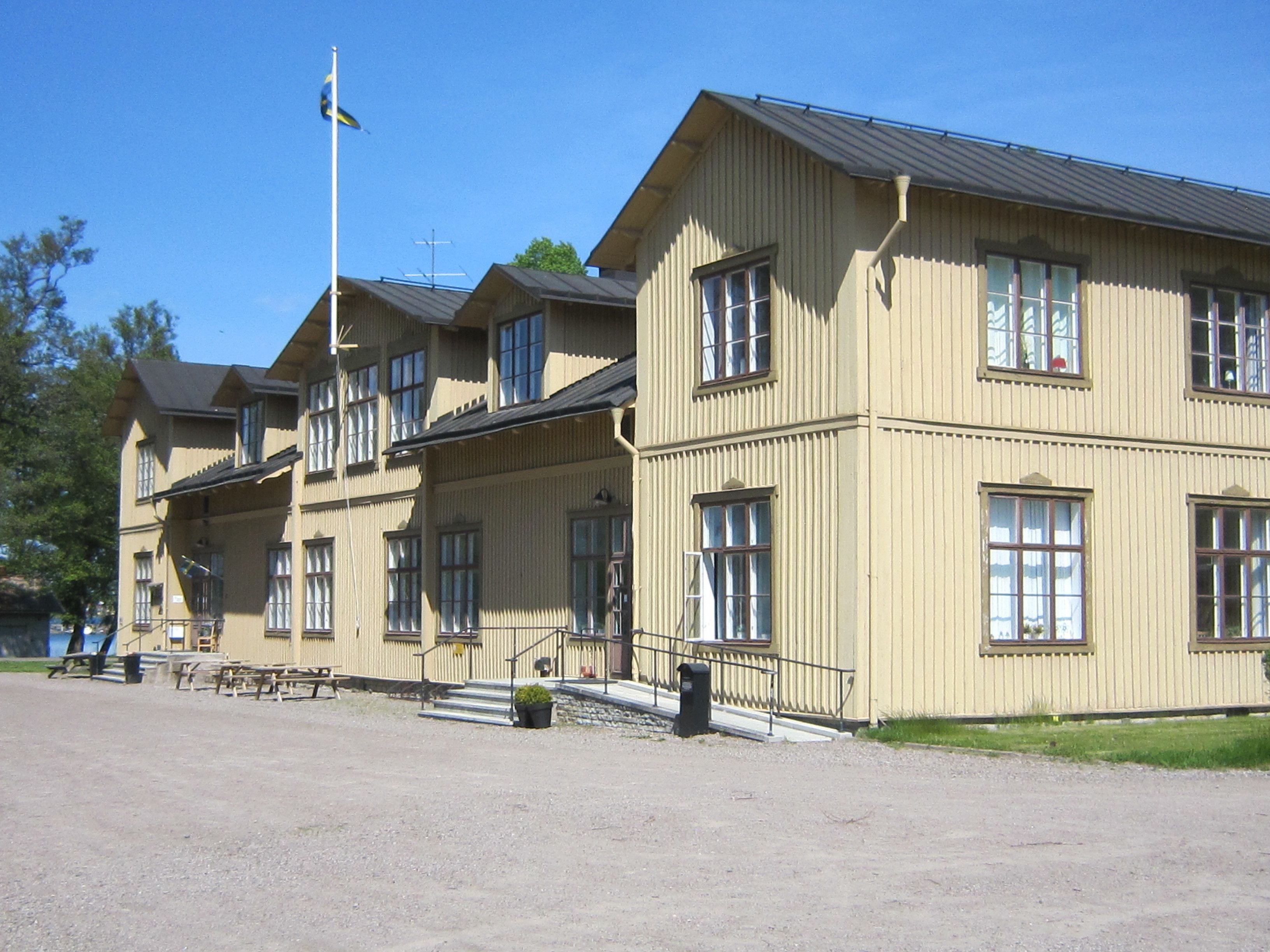 A row of beige wooden buildings with multiple windows and a flagpole.