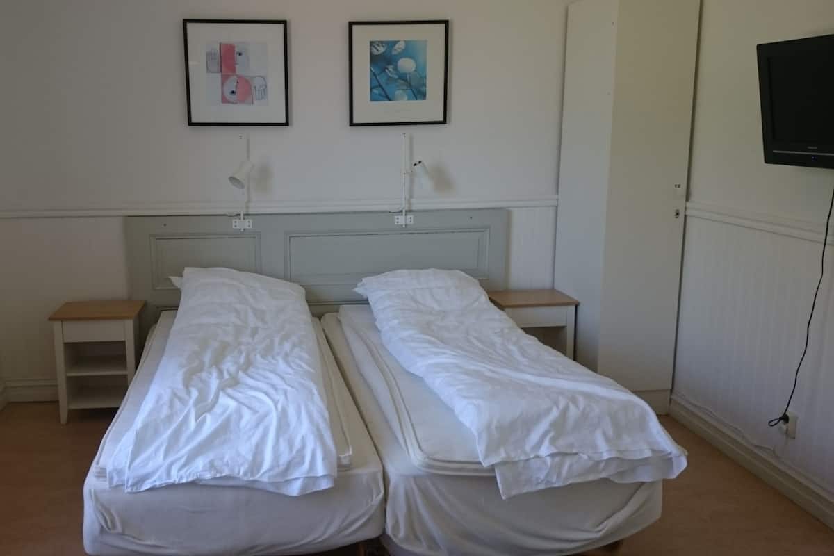 Une chambre avec deux lits simples, une petite table de chevet à côté de chaque lit, une tête de lit et un téléviseur fixé au mur.