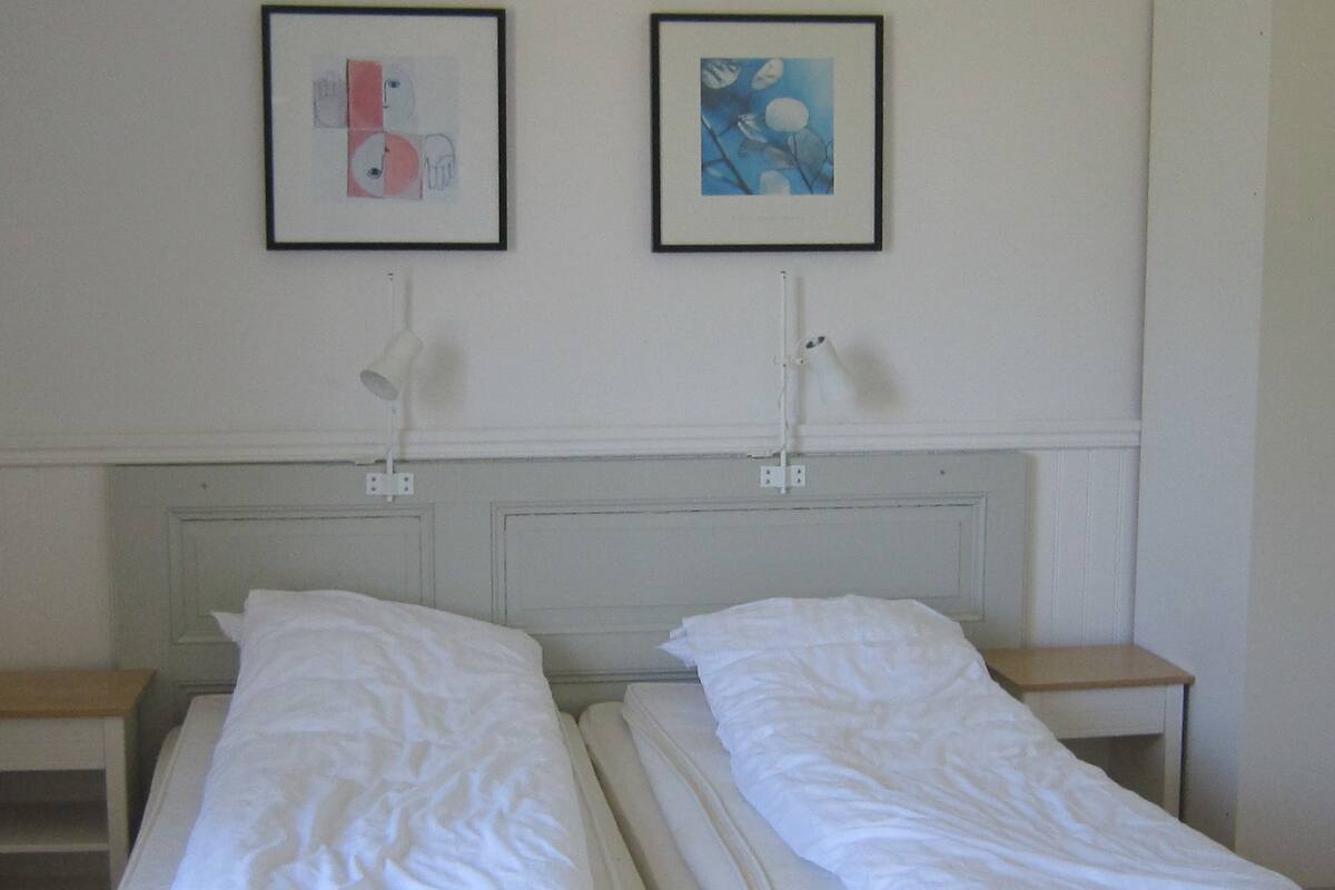 Une chambre avec deux lits simples, une literie blanche, une tête de lit blanche et deux tableaux encadrés au mur.