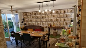 A dining area with a wooden table, chairs, a bookshelf, and a kitchen counter with food items. - B&B Cristiano (Rende)